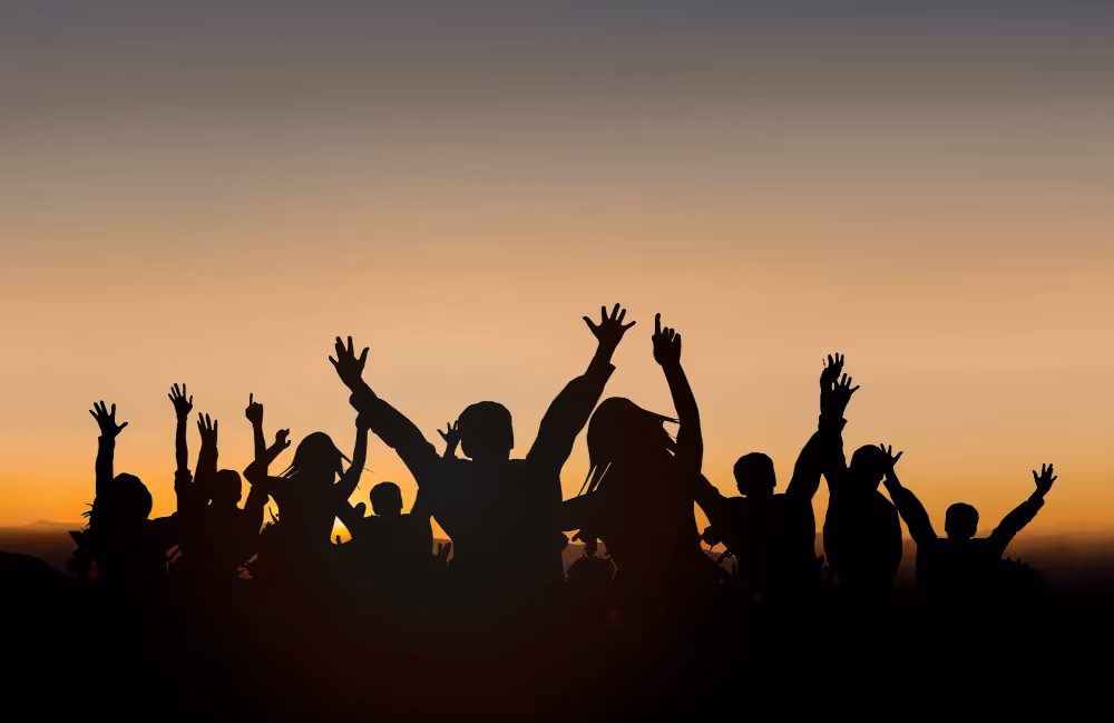 Silhouettes of a group of people with raised hands against a sunset sky.