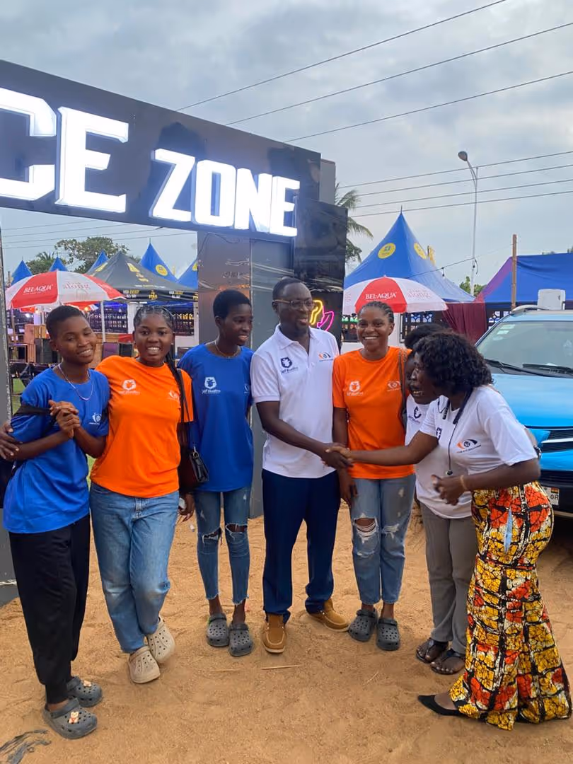 Group of six people standing and smiling outdoors near an illuminated sign reading 'ZONE,' with two individuals shaking hands.