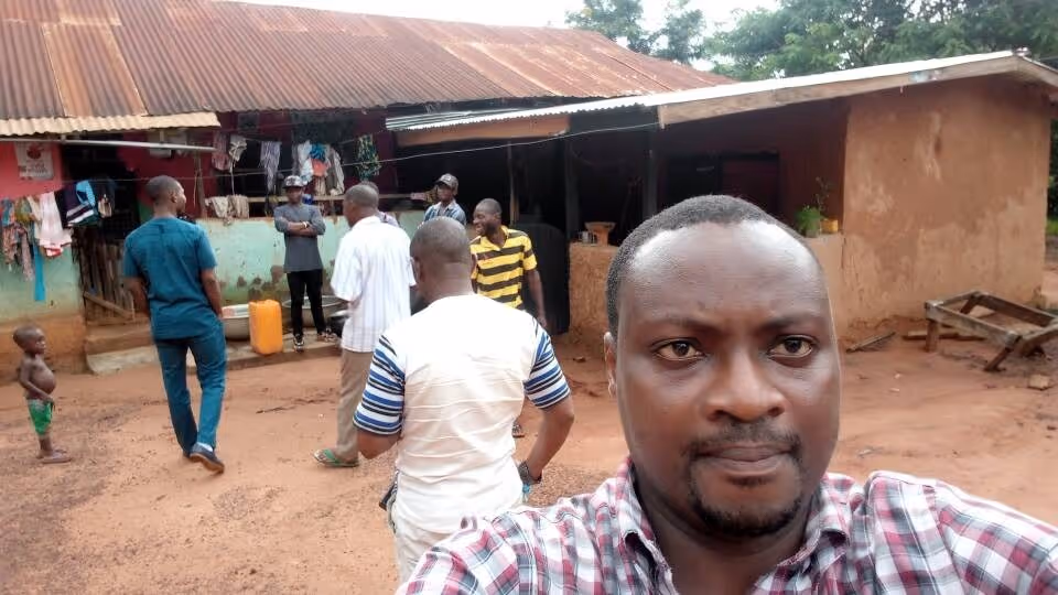 Group of men standing and talking outside a rustic building with a rusted corrugated metal roof.